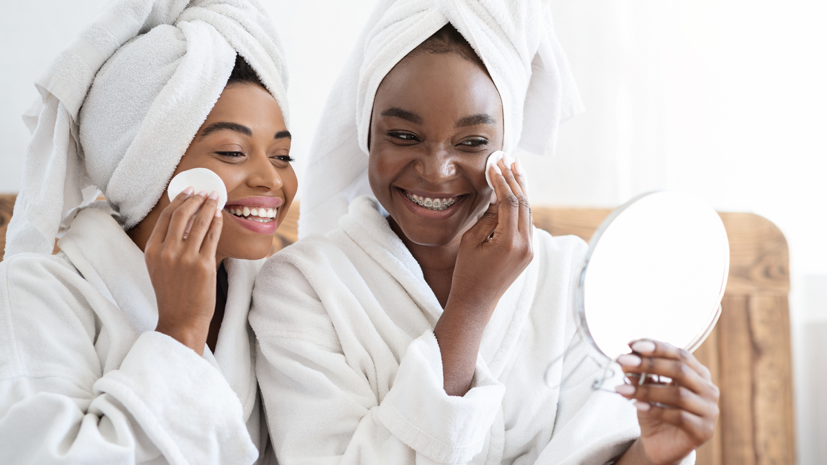 Zwei Junge Frauen im Bademantel tragen Toner Pads auf ihr Gesicht auf, betrachten sich im Spiegel