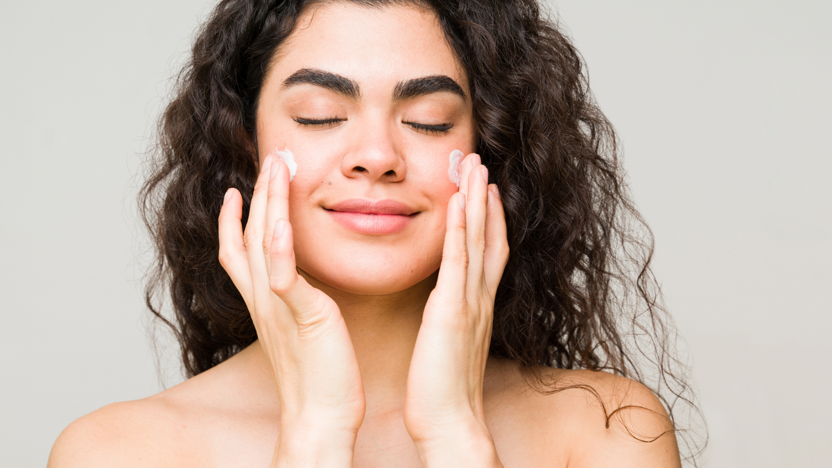 Nahaufnahme einer Frau mit locken trägt Sonnencreme auf ihren Wangen auf