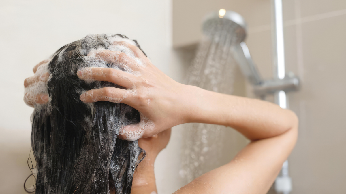 Frau wäscht ihre Kopfhaut unter der Dusche mit Shampoo