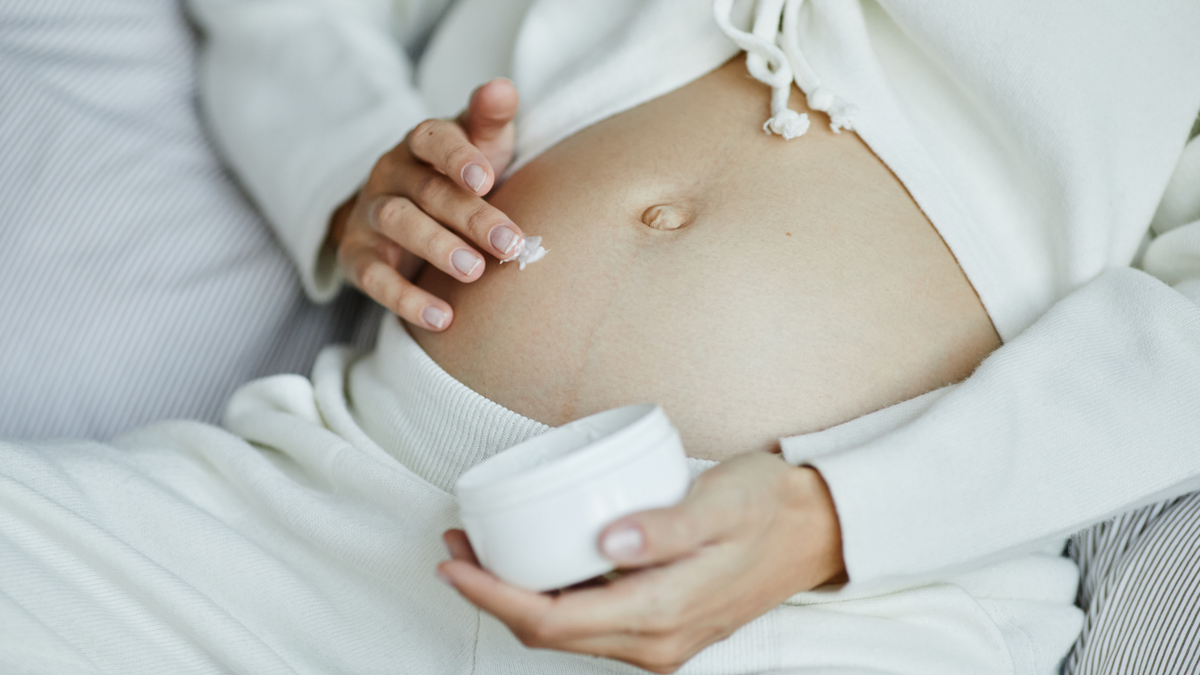 Schwangerschaftsbauch wird mit einer Feuchtigkeitscreme eingecremt