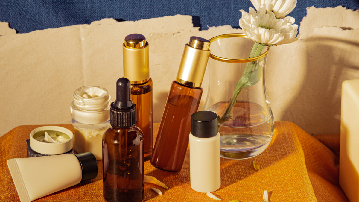 Sechs Skincare Produkte in braunen Farben neben einer Blume