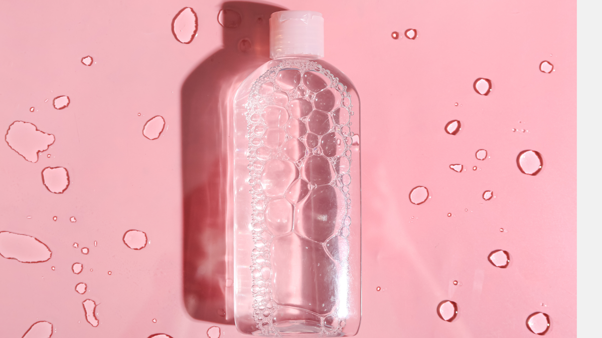 Flasche Mizellenwasser daneben Tropfen auf pinkem Hintergrund
