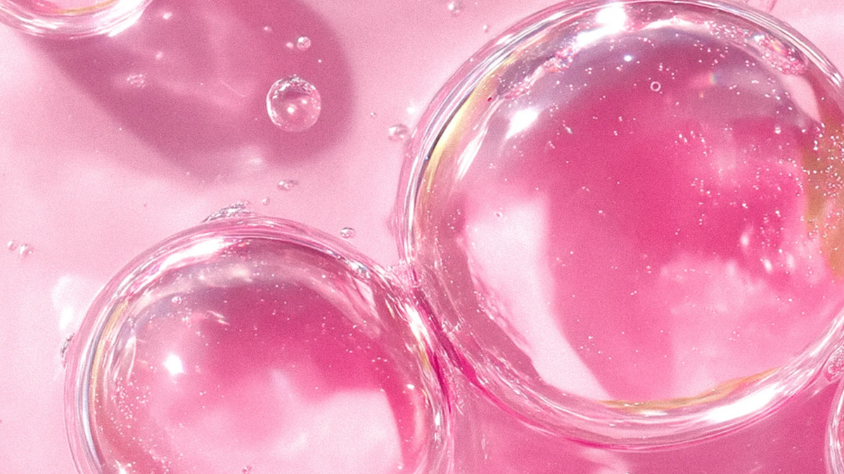 Transparente Blasen aus einem Serum vor einem pinken Hintergrund