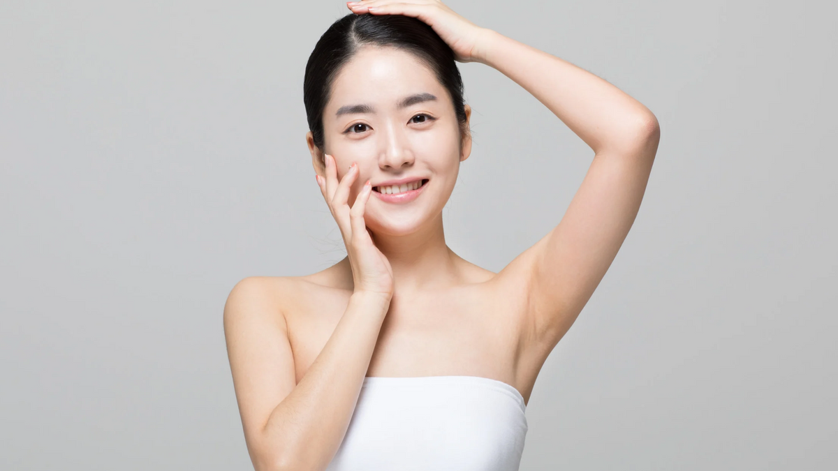 Foto einer jungen koreaischen Frau die in die Kamera lächelt und ihre Arme an ihr Gesicht hält