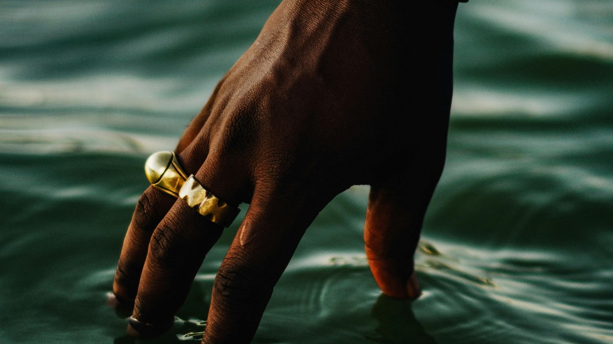 Hand mit zwei goldenen Ringen berührt die Wasseroberfläche