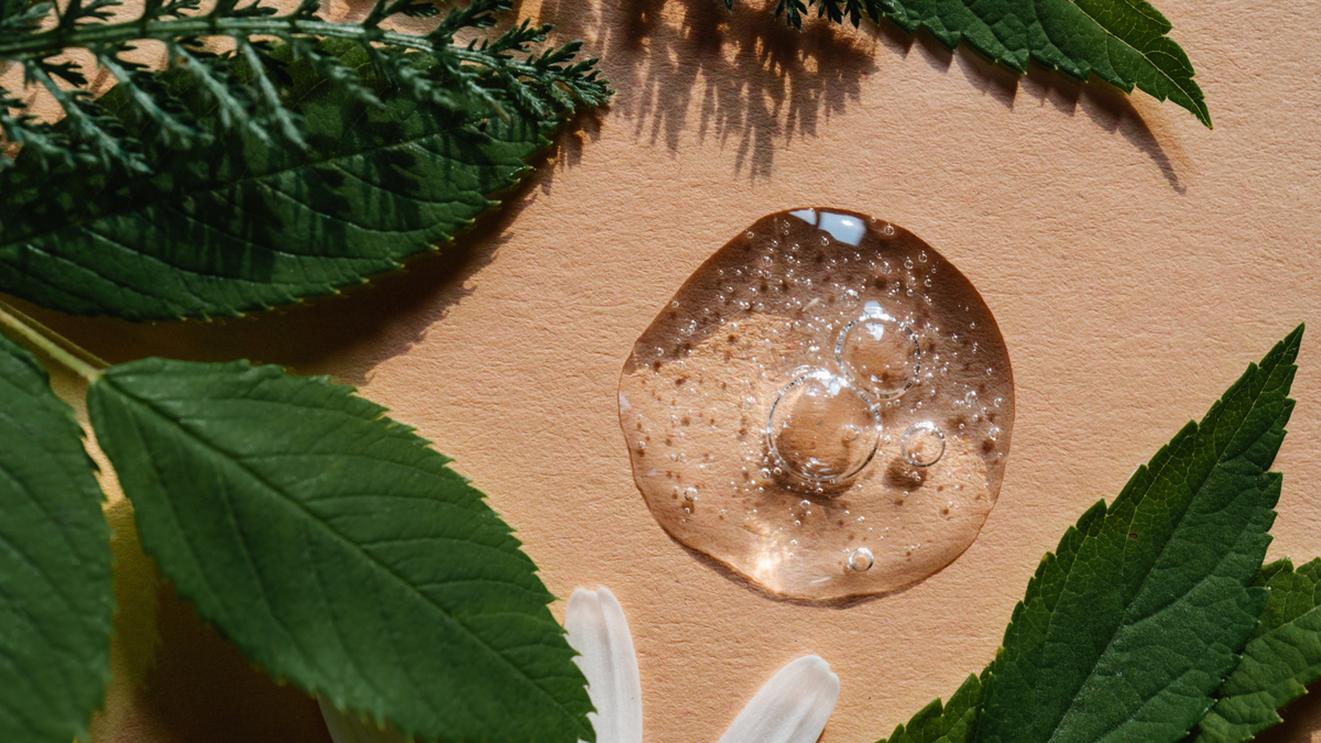 Gelartige Skincare-Textur auf hautfarbenem Hintergrund umgeben von Blättern