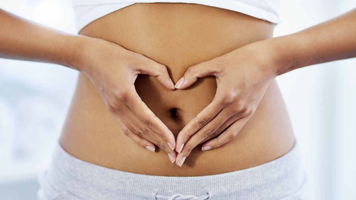 Eine Frau hält ihre Hände in Form eines Herzens vor ihren Bauch