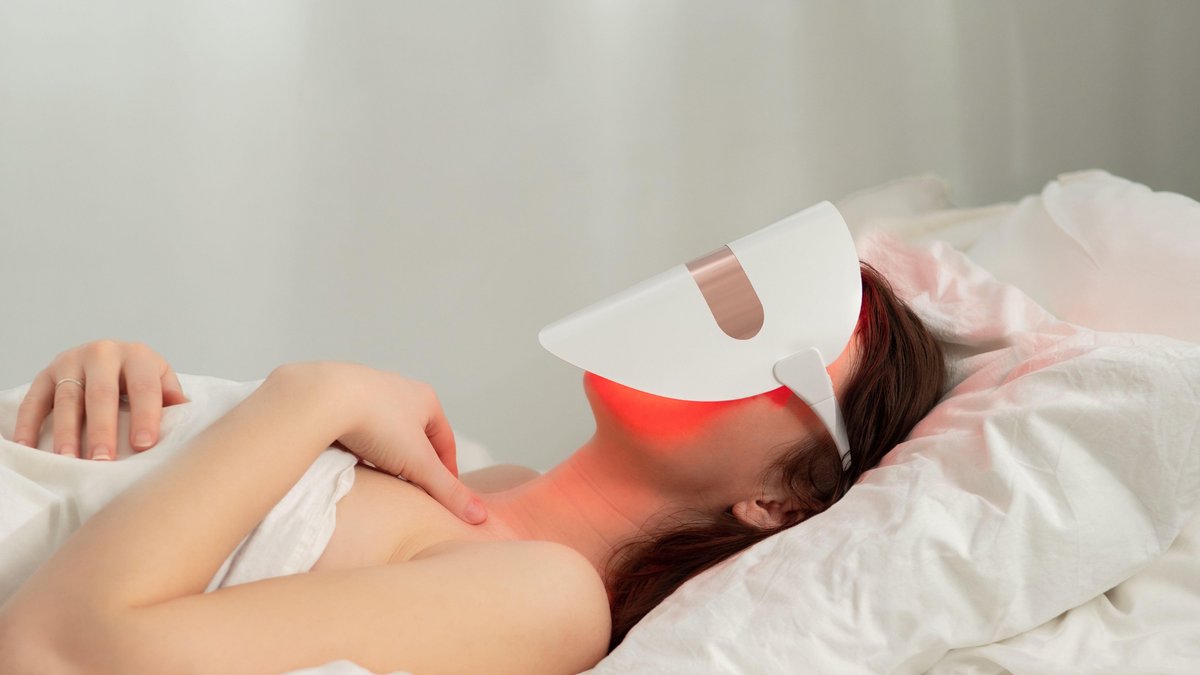 Eine junge Frau liegt im Bett und trägt eine LED Gesichtsmaske