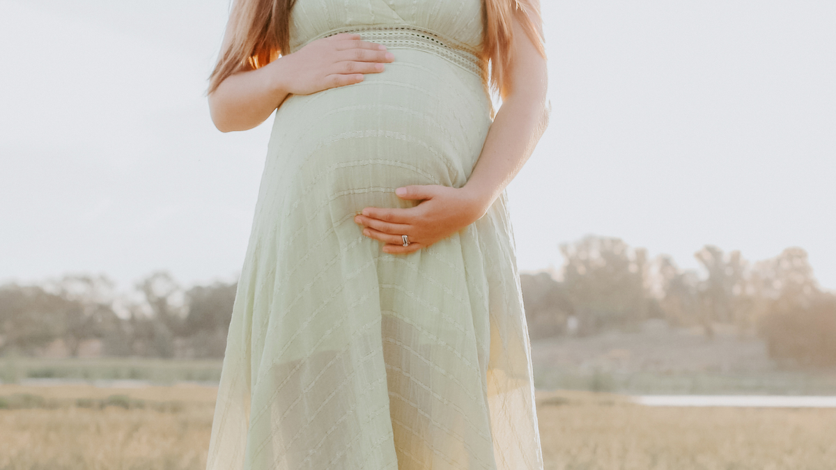 Schwangere Frau in einem mintfarbenen Kleid hält ihren Bauch 